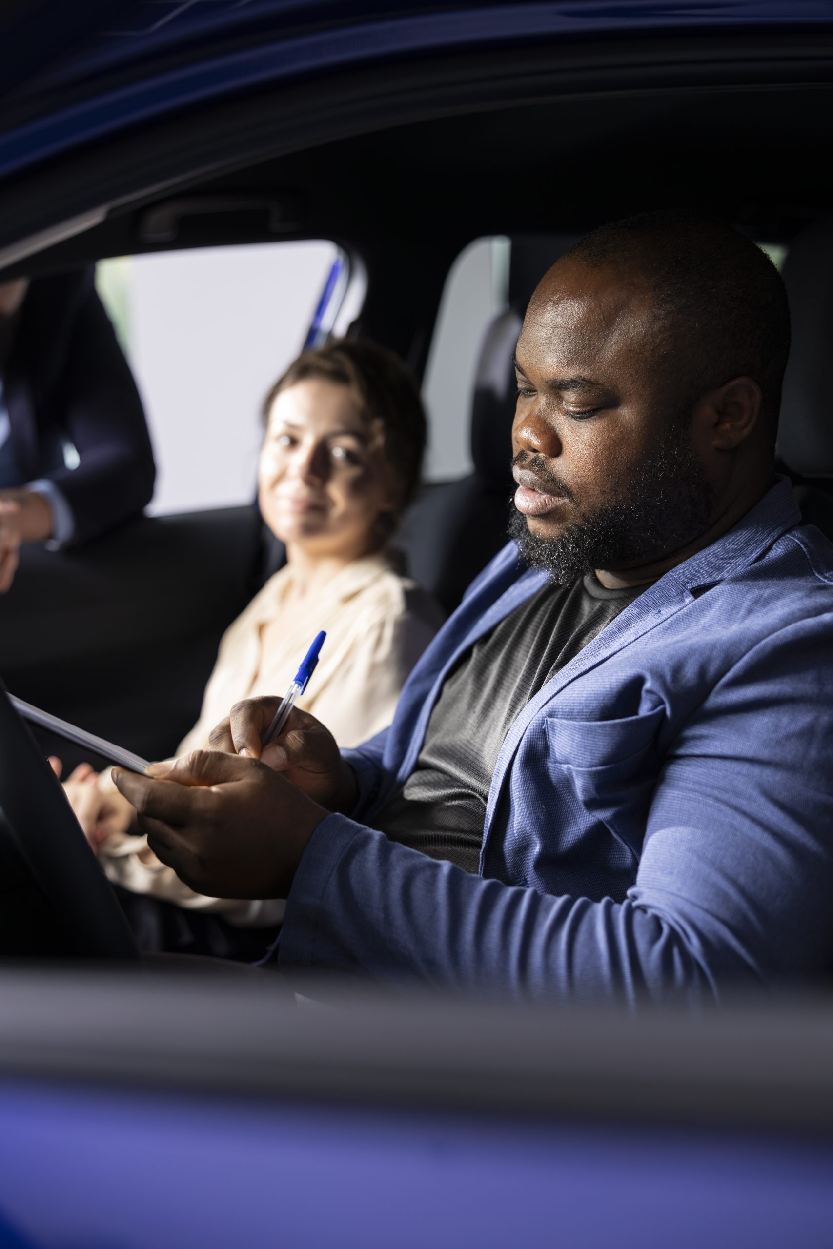 Couple in car dealership filling purchase paperwork after agreeing terms with salesman during test drive. Close up of showroom employee giving sale contract for african american client to sign